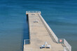 © John_Doo78 - Scenic high-angle view of a concrete pier stretching into calm blue water, featuring minimalist benches, white railings, and a 'no diving' sign on a sunny day