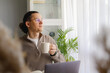 © Ina - Middle aged man enjoying coffee break while working remotely near bright window. Peaceful pause, work life balance, productivity and calm home office routine concept.