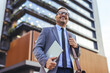© Dragana Gordic - Confident Businessman Carrying Laptop and Leather Bag Outside Modern Office Building During Commute