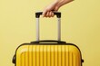 © Maryna - Hand holds bright yellow travel suitcase against solid yellow background. Ready for journey or vacation trip. Minimalist style conveys excitement for adventure and departure.