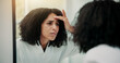 © peopleimages.com - Woman, concern and check face in mirror with skincare, inspection or fear for acne breakout in bathroom. Female person, skin evaluation and dermatology in house with reflection, worry or pimple issue