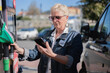 © ADDICTIVE STOCK - Senior woman refueling car checking phone