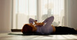© Binzari - In a bright living room, a woman engages in stretching and pilates exercises on a mat. The sunny space promotes a healthy morning routine filled with movement.