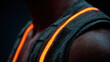 © Chaiwit - Close up of dark skin shoulder with reflective safety vest glowing orange light in low light environment, highlighting texture and fabric detail