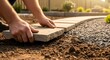 © tembok - Hands laying paving stone pathway outdoors.