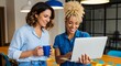 © White Craft  - Two women collaborate over a laptop at a bright desk. One holds a blue mug, the other taps the screen. Modern interior features warm lighting and colorful decor. Their smiles suggest teamwork