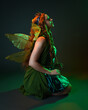 © faestock - portrait of female model wearing fantasy fairy costume, green dress, cloak, butterfly wings and crown. full length sitting pose, kneeling on floor, dark studio background.