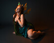 © faestock - portrait of female model wearing fantasy fairy costume, green dress, cloak, butterfly wings and crown. full length sitting pose, kneeling on floor, dark studio background.