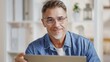 © nyul - Portrait of middle aged man sitting at desk in bright room working with laptop computer in home office. Mature age, middle age, mid adult casual man in 50s, confident happy smiling.