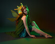 © faestock - portrait of female model wearing fantasy fairy costume, green dress, cloak, butterfly wings and crown. full length sitting pose, kneeling on floor, dark studio background.