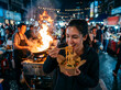 © akirra28 - Person Eating Noodles with Chopsticks at Night Market with Wok Fire Background