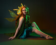 © faestock - portrait of female model wearing fantasy fairy costume, green dress, cloak, butterfly wings and crown. full length sitting pose, kneeling on floor, dark studio background.