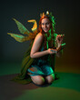 © faestock - portrait of female model wearing fantasy fairy costume, green dress, cloak, butterfly wings and crown. Full length kneeling pose holding secret jewellery box, isolated on dark studio background