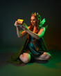 © faestock - portrait of female model wearing fantasy fairy costume, green dress, cloak, butterfly wings and crown. Full length kneeling pose holding secret jewellery box, isolated on dark studio background