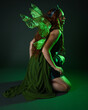 © faestock - portrait of female model wearing fantasy fairy costume, green dress, cloak, butterfly wings and crown. full length sitting pose, kneeling on floor, dark studio background.