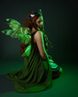 © faestock - portrait of female model wearing fantasy fairy costume, green dress, cloak, butterfly wings and crown. full length sitting pose, kneeling on floor, dark studio background.