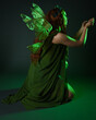 © faestock - portrait of female model wearing fantasy fairy costume, green dress, cloak, butterfly wings and crown. full length sitting pose, kneeling on floor, dark studio background.