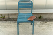 © Pablo - Modern teal metal chair with a leather journal on the seat placed outdoors against a industrial wall