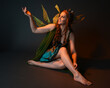 © faestock - portrait of female model wearing fantasy fairy costume, green dress, cloak, butterfly wings and crown. full length sitting pose, kneeling on floor, dark studio background.