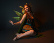 © faestock - portrait of female model wearing fantasy fairy costume, green dress, cloak, butterfly wings and crown. full length sitting pose, kneeling on floor, dark studio background.
