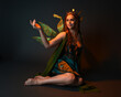 © faestock - portrait of female model wearing fantasy fairy costume, green dress, cloak, butterfly wings and crown. full length sitting pose, kneeling on floor, dark studio background.
