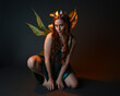 © faestock - portrait of female model wearing fantasy fairy costume, green dress, cloak, butterfly wings and crown. full length sitting pose, kneeling on floor, dark studio background.