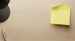 © Banstanks - Yellow sticky note on wooden surface with pen and lamp in a top view composition