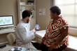 © Seventyfour - Black middle aged woman consulting male doctor, reviewing glucose monitoring app on smartphone during clinic visit. Useful for telehealth, chronic care management, patient engagement marketing