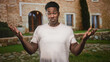 © Krakenimages.com - Man shrugging with palms up and later crossing arms in front of a stone building with arched doorway and cypress tree; uncertainty.