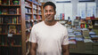 © Krakenimages.com - Man smirks standing by stacked books and tall bookshelves, casual pose in a bookstore building; amused casual confidence.