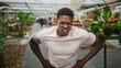 © Krakenimages.com - Man clutching lower back and stomach, grimacing amid indoor plant market inside a building; pain urgency.
