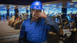 © Krakenimages.com - Man construction worker in blue hardhat and blue coveralls wiping his eye with hand in building gym cardio area; fatigue resilience determination.