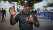 © Krakenimages.com - Man police officer raises right hand and places left hand on chest while wearing dark uniform, cap, badge and radio on a busy city street; duty pledge.