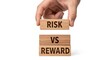 © Shakib - Hand stacking wooden blocks risk vs reward text on white background.
