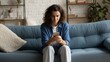 © Olly Photography - A woman in casual attire using a smartphone while sitting on a cozy blue sofa in a modern living room.