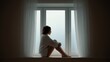 © Sipan - Person sitting on a wide window sill with knees drawn to chest, evoking quiet vulnerability and emotional introspection.