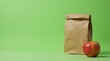 © Alex Pios - Wellbeing focused lunch scene with brown bag and ripe apple set on green backdrop