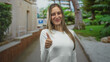 © Krakenimages.com - Young hispanic woman giving thumbs up with visible hand standing on a street by a park building; joyful.