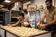 © ADDICTIVE STOCK - Bakers glazing dough pieces in an artisan bakery kitchen
