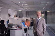 © .shock - Experienced Arab businessman standing confidently in a modern open office with diverse startup team