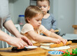 © JackF - Toddler children help mom cook pizza. Family activity for development of fine motor skills. Child lays out pieces of bacon on pizza base dough.