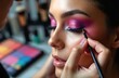 © Vadym - Makeup artist applies vibrant pink purple eyeshadow to eyelid. Woman gets eye makeup, beauty service. Skilled hands use brush, cosmetic palette.