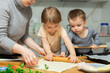 © JackF - Toddler children help mom cook pizza. Family activity for development of fine motor skills. Child lays out pieces of bacon on pizza base dough.