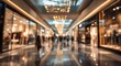 © Ria - A blurred perspective of a bustling shopping mall corridor filled with people and bright lights.