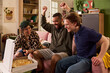 © pressmaster - Multiethnic friends celebrating shared success while gathering around pizza at home, expressing friendship and student lifestyle. Ideal for youth culture, campus life, social bonding marketing
