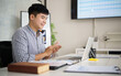 © matinee - Happy businessman clapping hands while working on a laptop, celebrating success and positive results in a modern office.