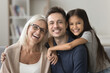 © fizkes - Attractive multigenerational family posing for photo at home seated on couch, looking at camera with positive and joyful expression, enjoy their harmonic relationships, understanding and time together