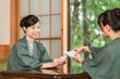 © buritora - A woman and her friend drinking sake on the veranda of a Japanese-style room in a traditional Japanese inn, both wearing yukata robes.