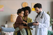 © DragonImages - African American mother holding child while doctor showing tablet during home visit, discussing pediatric care and treatment