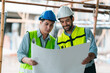 © chokniti - Construction worker review plan in site interior, two engineer in safety helmet and vest reading blueprint with focused teamwork